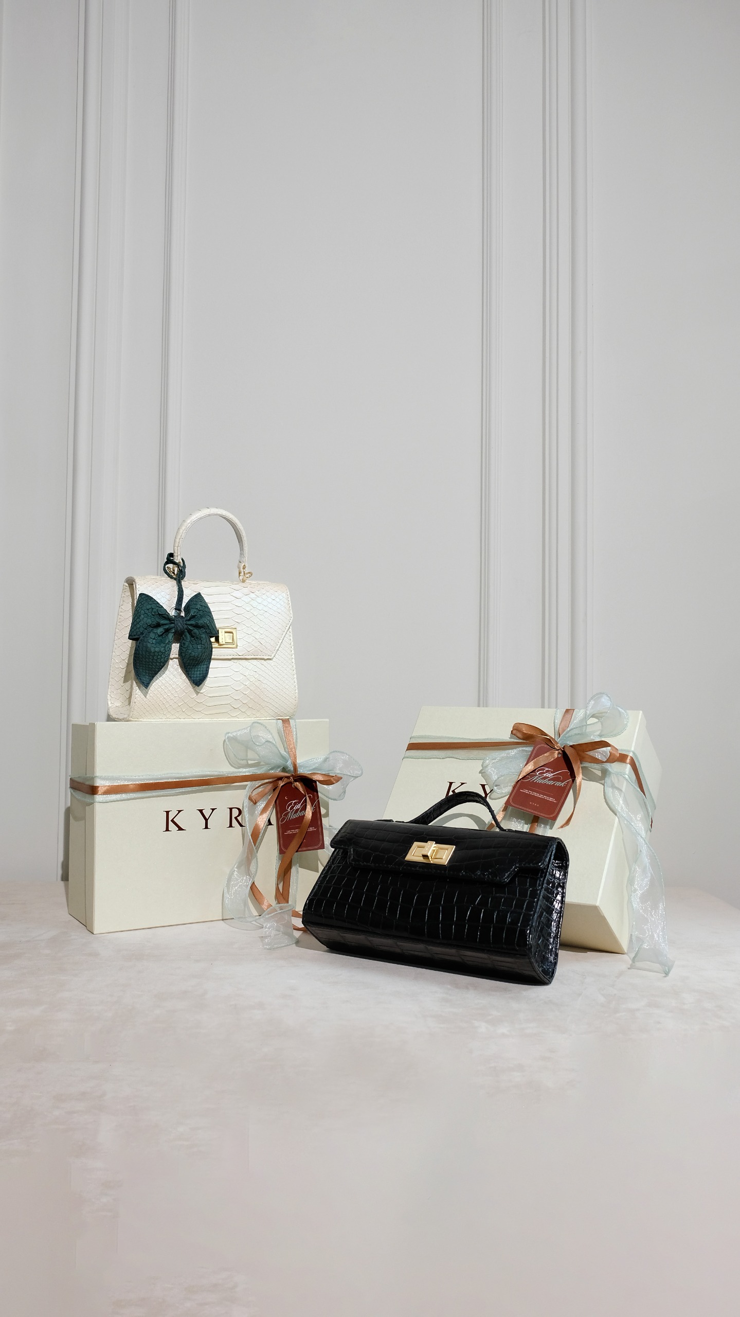 Kyra Eid 2026 hampers featuring a white lizard leather Adriana bag and a black crocodile leather handbag in premium gift boxes.