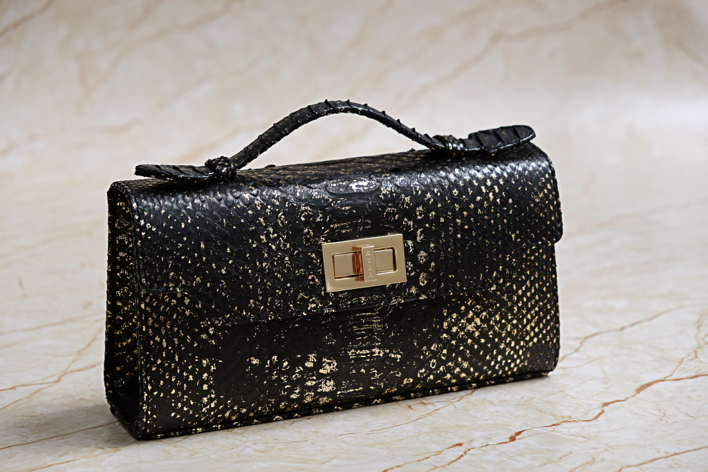 KYRA Luna 25 structured black python leather handbag with artistic gold-brushed accents, gold hardware signature lock, and detachable shoulder strap for Eid 2026.