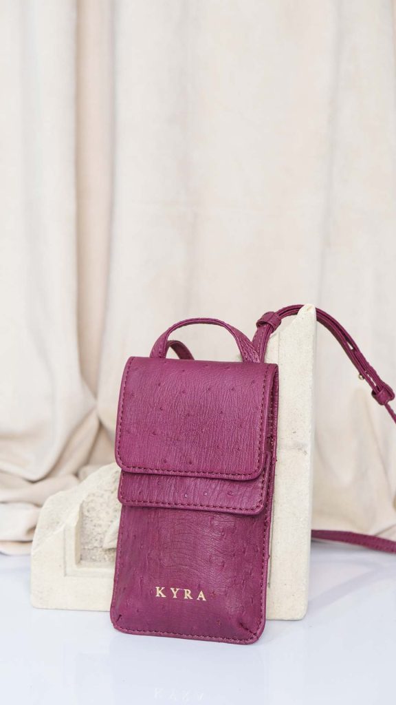 KYRA Phone Bag in genuine ostrich leather featuring a vertical minimalist silhouette, gold hardware accents, and a versatile 3-way strap for crossbody or belt bag styling.