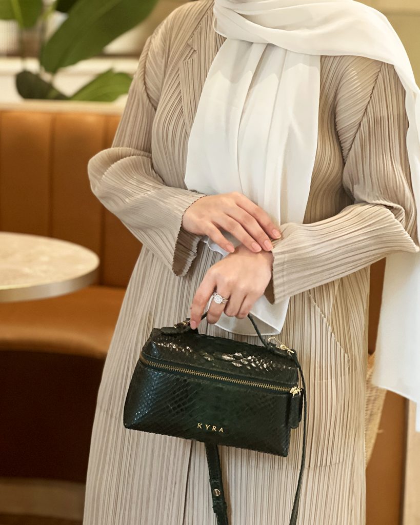 Woman holding KYRA Picco Bag in Hunter Green genuine python leather with gold hardware, styled with a beige pleated abaya and white hijab — exotic leather bag perfect for Eid Adha 2026