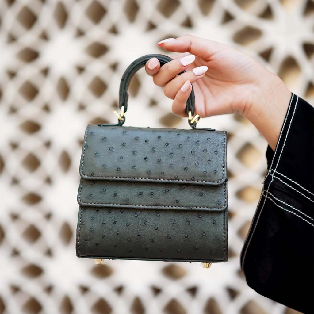 Rubby small hunter green ostrich leather handle bag with a unique layering closure and distinct quill patterns held by a hand.
