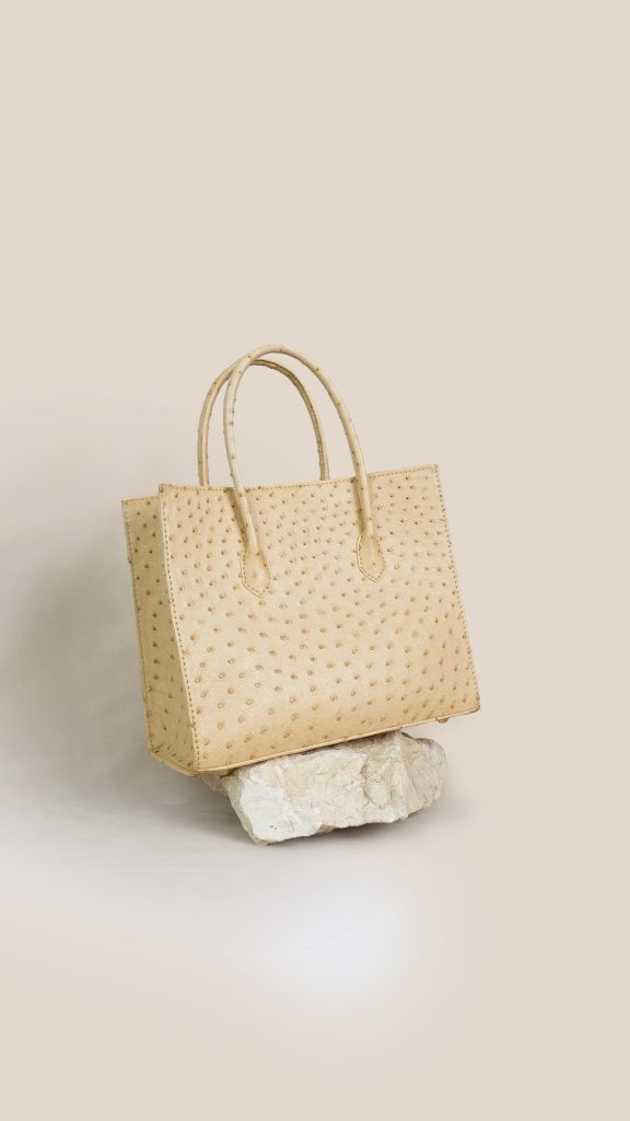 A structured luxury KYRA Roomy tote bag crafted from premium peanut brown ostrich leather with distinct quill patterns and elongated top handles on a white background.